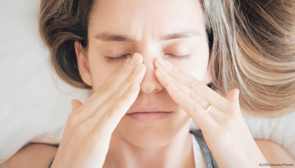 Mulher com olhos fechados, segurando nariz com as mãos.