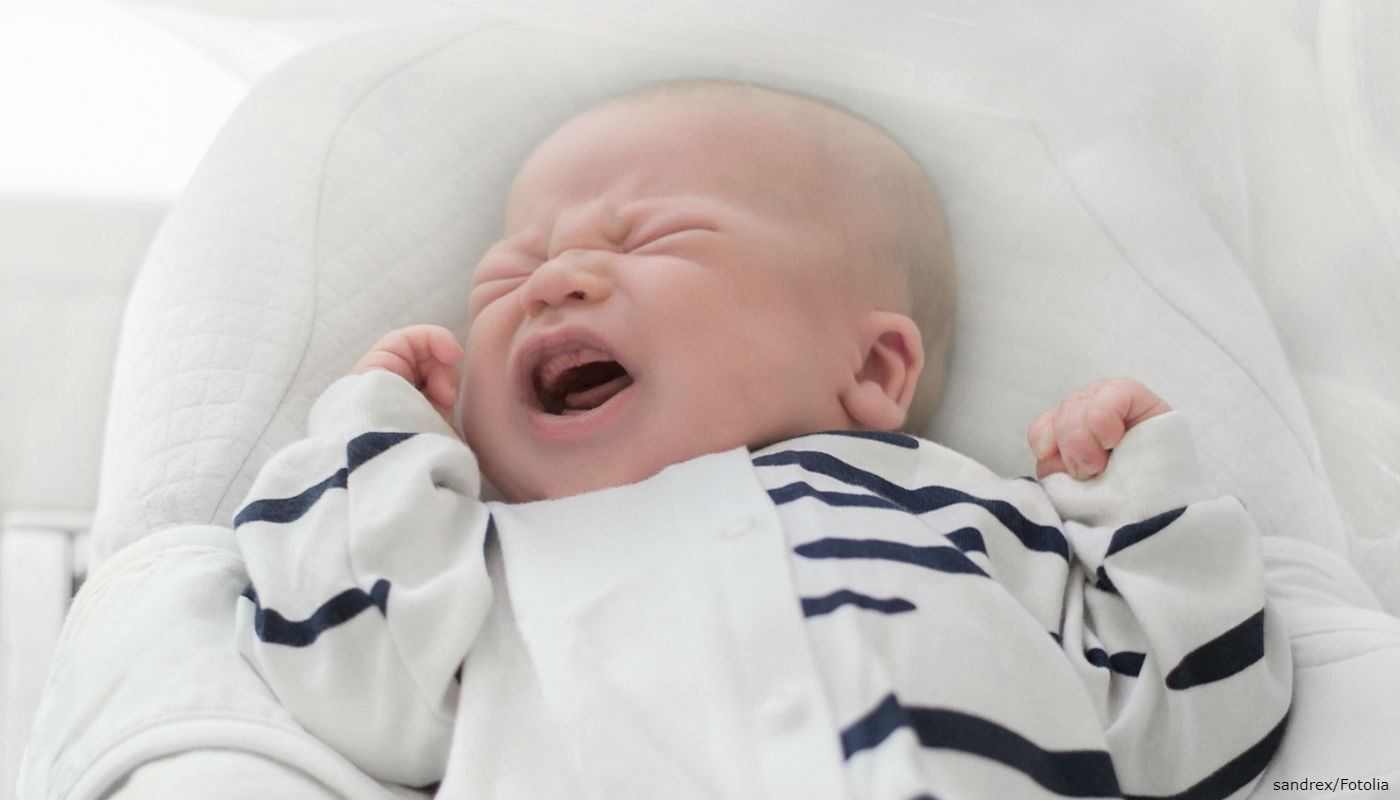 Bebê chorando com a mão no rosto.